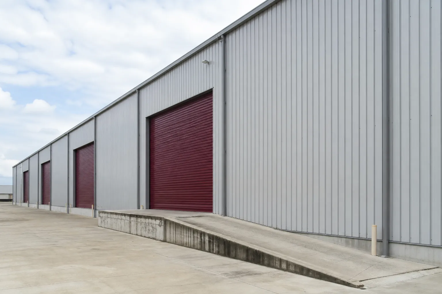 Façade latérale d’un bâtiment de stockage, plusieurs larges rideaux métalliques alignés